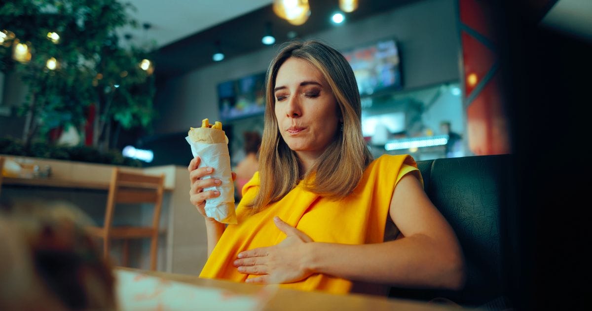 donna mangia un panino e si tiene la pancia con la mano perché ha la pancia gonfia